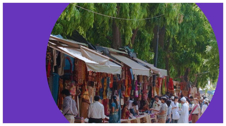 Colourful stalls with scarves bags and jewellery lining the walkway at janpath market delhi on a busy afternoon