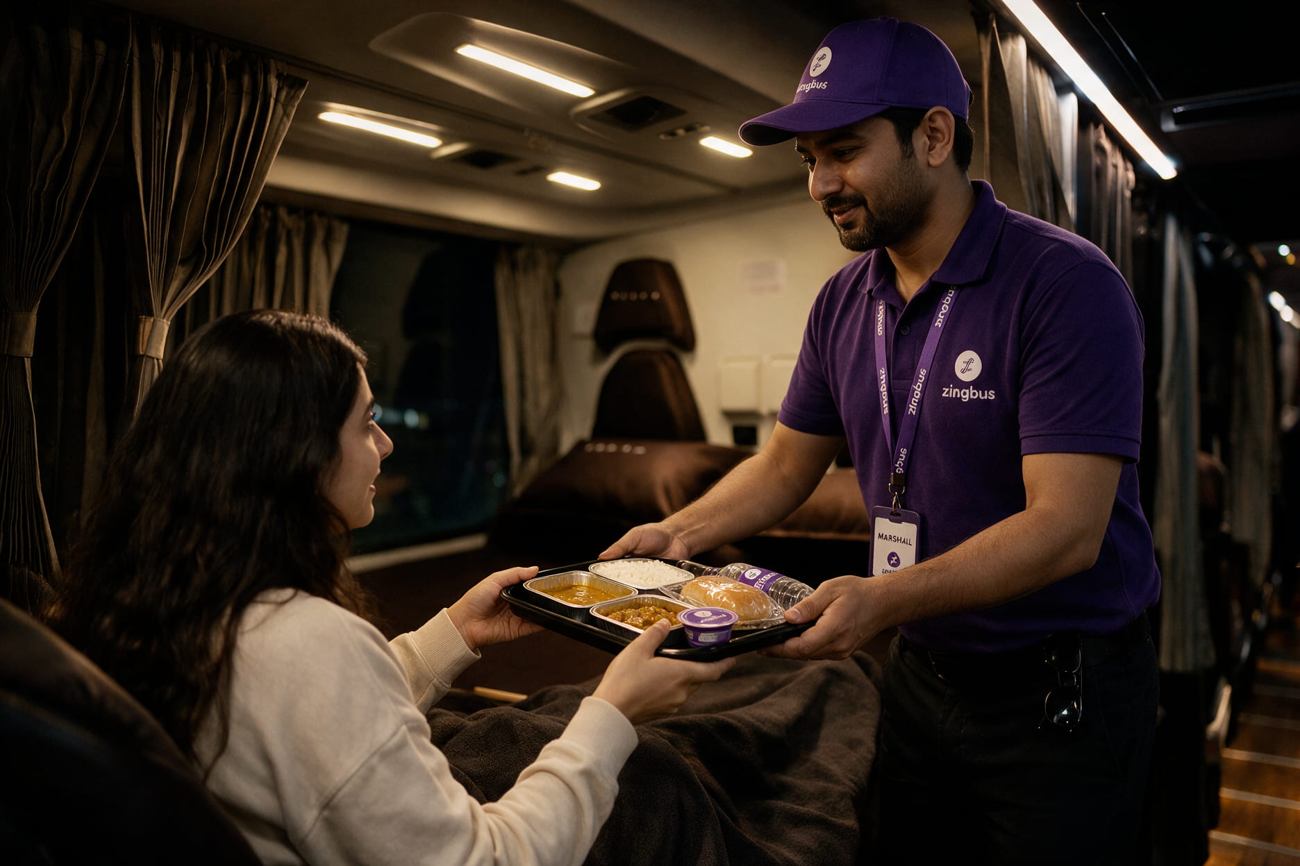 Passenger receiving a meal tray from an onboard marshal on a zingbus intercity coach at night