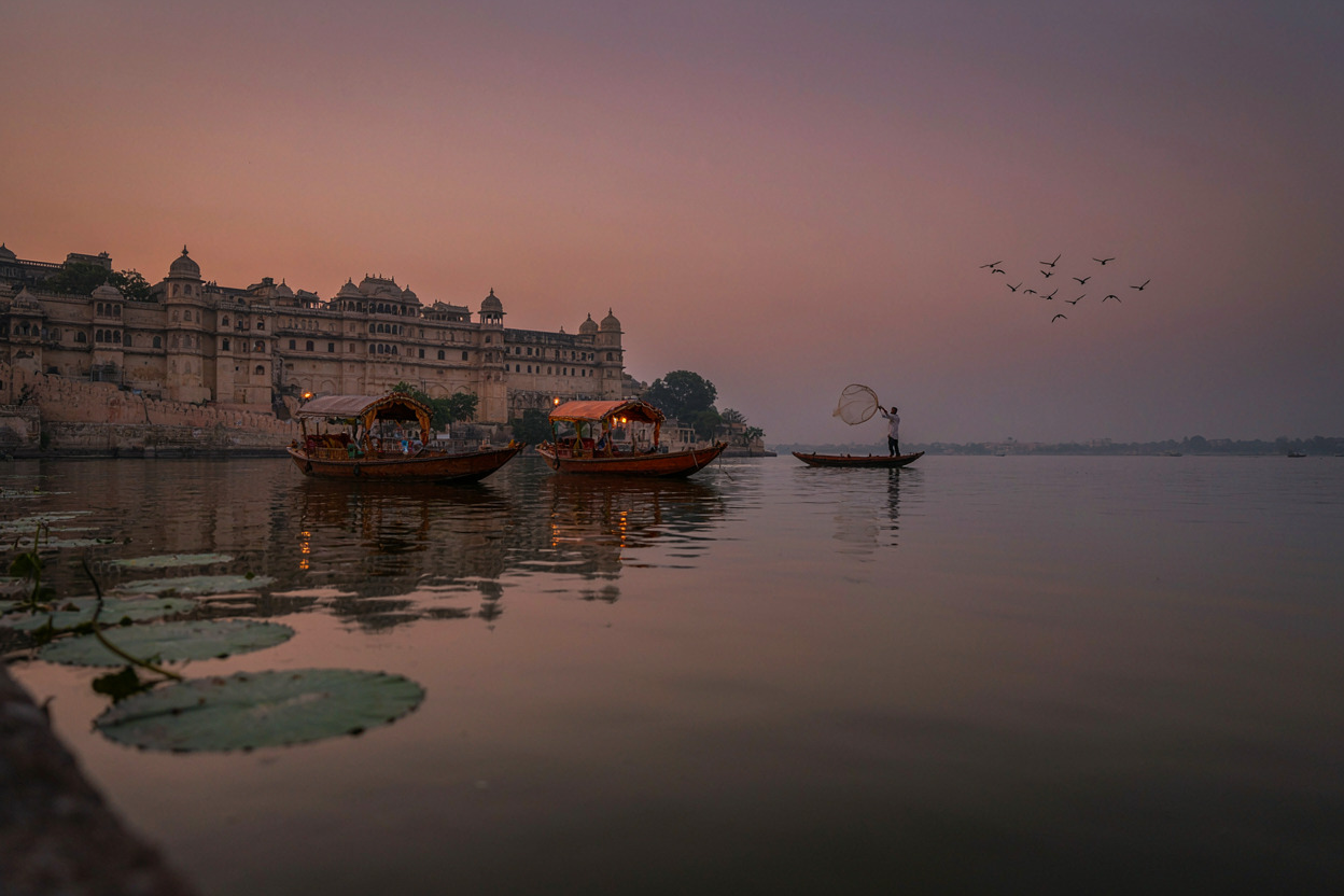 Boats on Lake Pichola in Udaipur with the City Palace walls along the shore at dusk